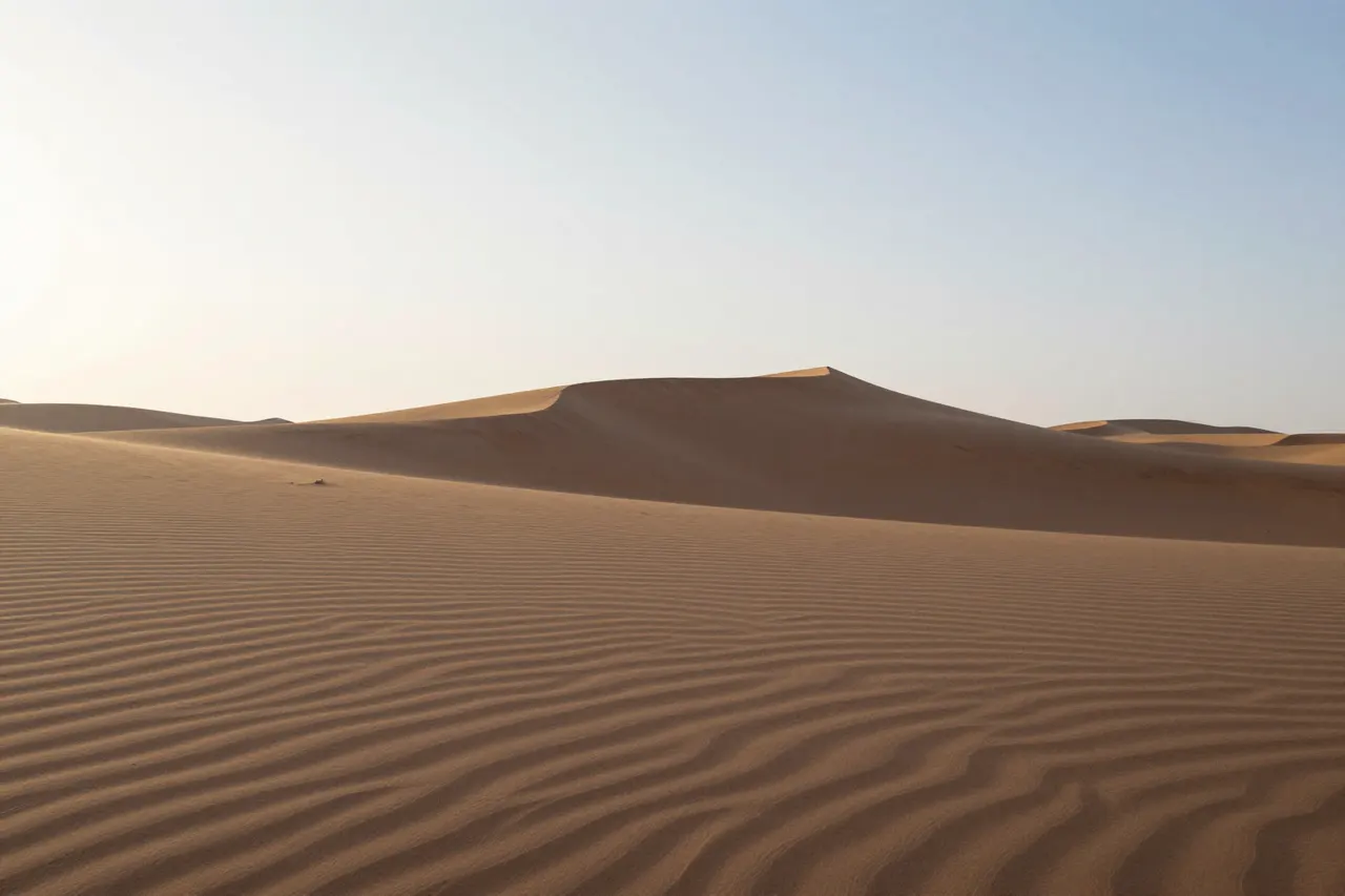 صورة توضيحية مولّدة بالذكاء الاصطناعي لـكثبان الصحراء عند الفجر. المشهد توضيحي ولا يمثل صورة فوتوغرافية للأصل.